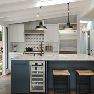 Two black pendant lights hang over a kitchen island with a wine fridge and bar stools