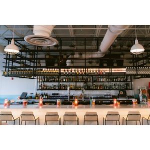 A modern bar interior features pendant lights hanging above a well-stocked bar
