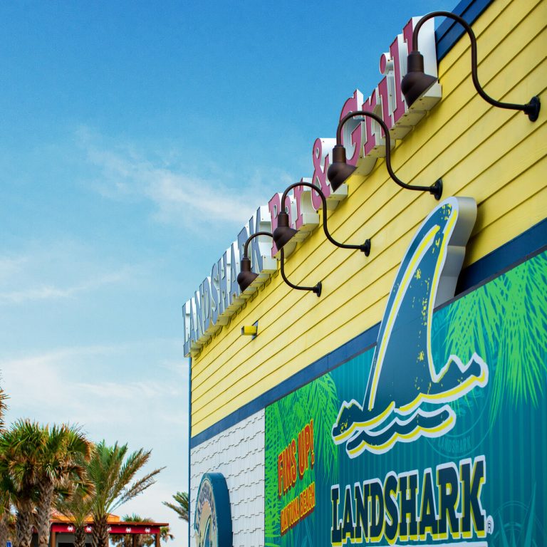 Four gooseneck wall lights illuminate the exterior of a yellow building with a Landshark sign