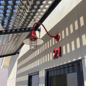 A red gooseneck barn light with a caged bulb is mounted on a textured wall next to the number 21