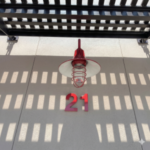 A red caged pendant light is mounted on a textured wall under a slatted roof