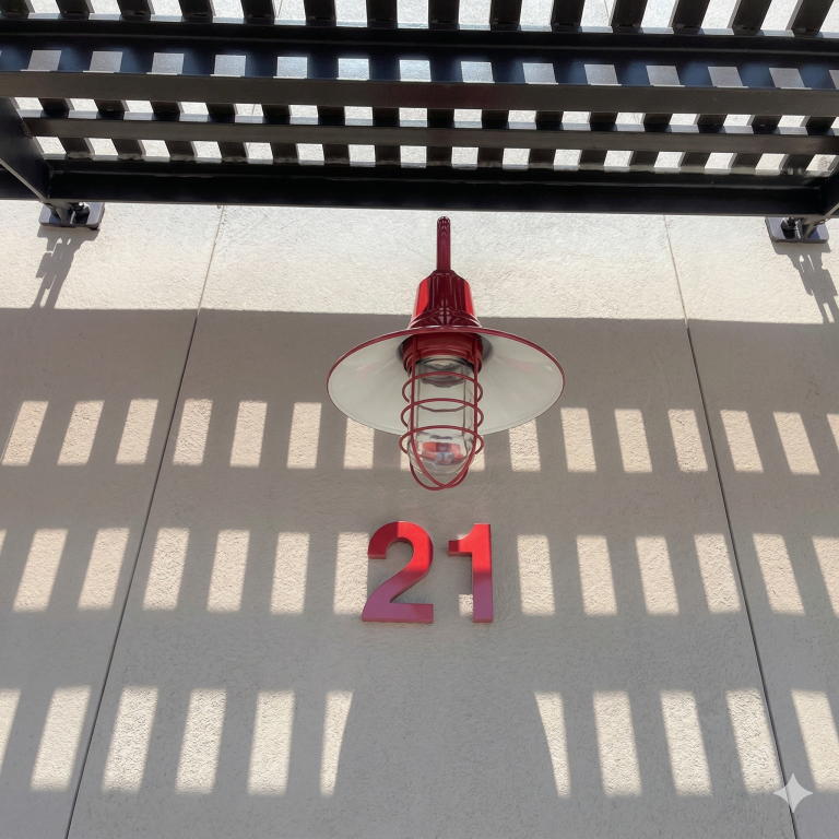 A red caged pendant light is mounted on a textured wall under a slatted roof