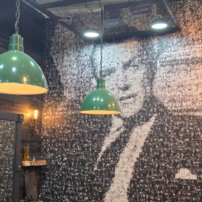 Two green pendant lights hang in front of a wall covered in a collage of black and white portraits