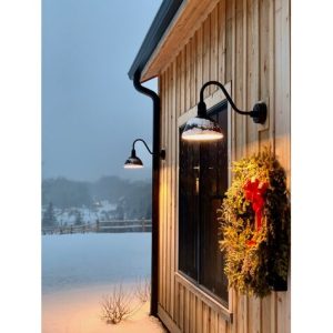 Two black gooseneck barn lights illuminate the exterior of a wooden building on a snowy day