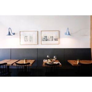 Two light blue gooseneck wall lights are mounted on a white wall above a dark grey banquette seating area in a restaurant