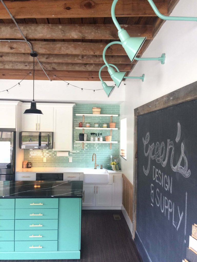 A modern kitchen features a teal island, subway tile backsplash, and industrial-style gooseneck wall lights