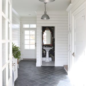 Two industrial-style pendant lights hang in a hallway with shiplap walls and dark tiled flooring