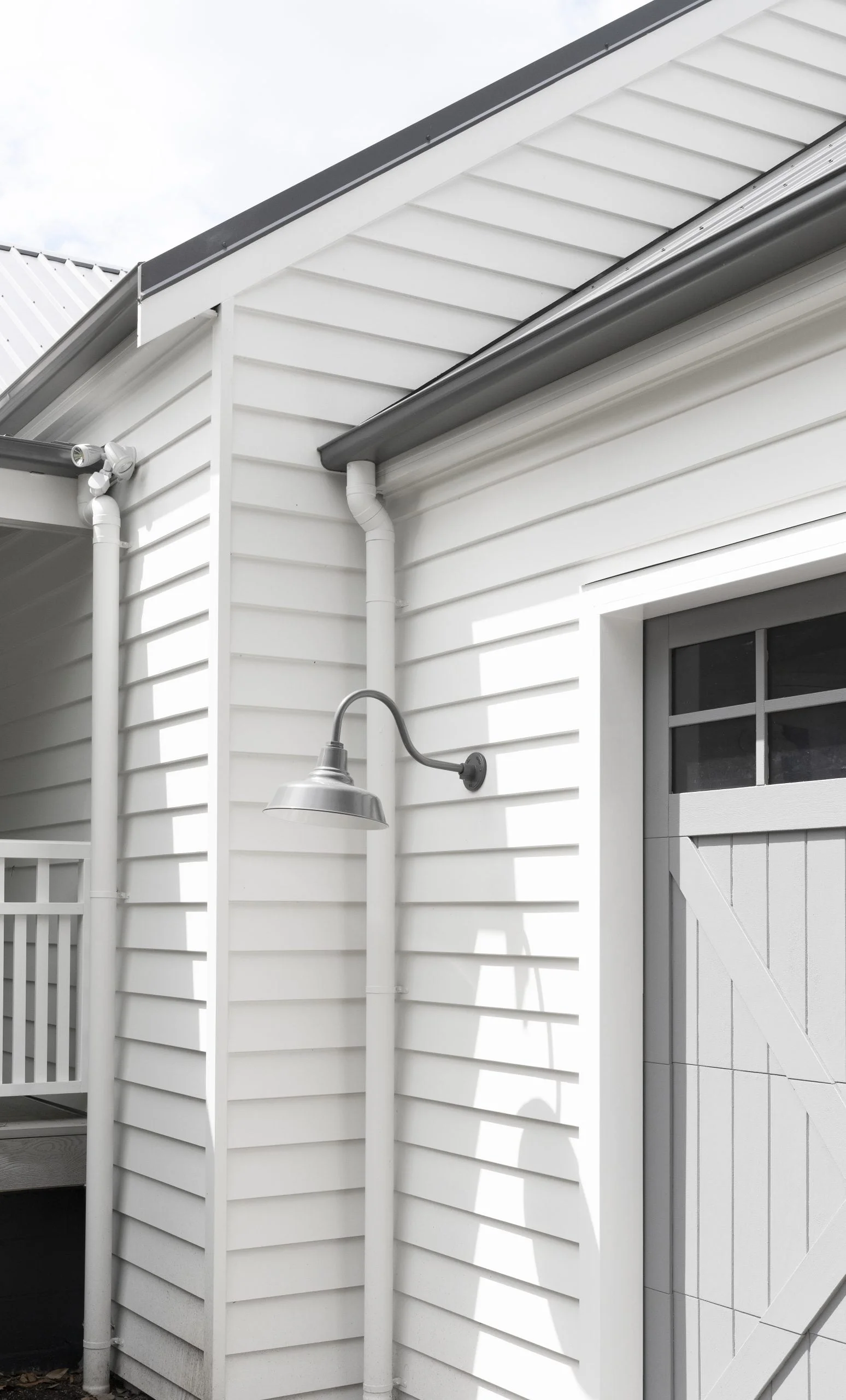 A grey gooseneck barn light is mounted on the white weatherboard exterior of a home