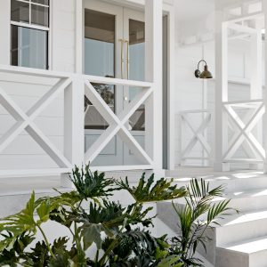 A modern white home features a gooseneck wall light illuminating the porch