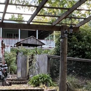 Three pendant lights hang from a wooden pergola in a garden setting