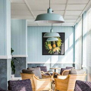 Two pendant lights hang above a seating area with wicker chairs and purple cushions