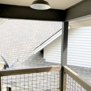 A dark barn-style pendant light hangs from a covered porch ceiling