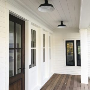 Two black barn-style pendant lights are mounted on the white ceiling of a covered porch