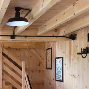 A black barn-style pendant light is mounted on a wooden ceiling above a staircase
