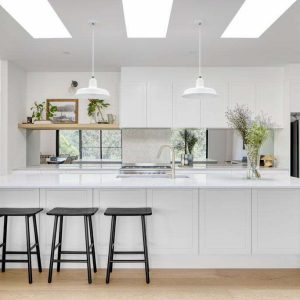Two white barn-style pendant lights hang above a large kitchen island in a modern white kitchen