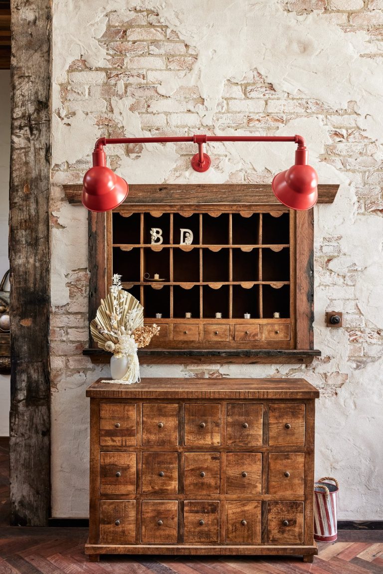 A rustic wooden dresser with a vintage pigeonhole cabinet above it is illuminated by a red industrial wall light