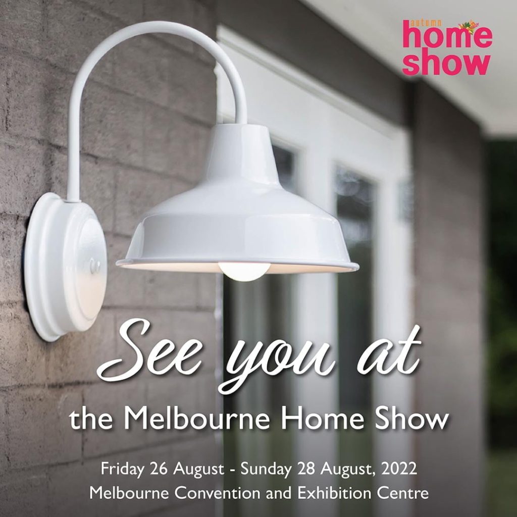 A white gooseneck wall light is mounted on a brick wall next to a door, advertising the Melbourne Home Show