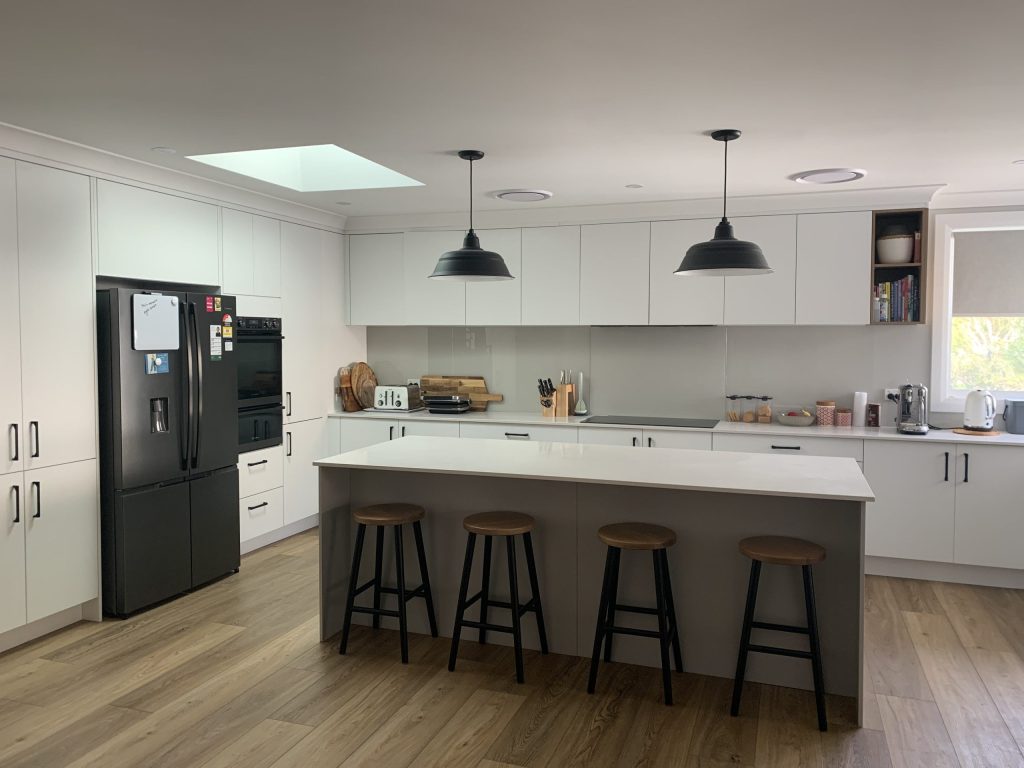 Two black pendant lights hang over a kitchen island in a modern kitchen with white cabinetry