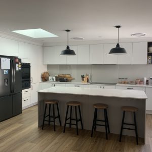 Two black pendant lights hang over a kitchen island in a modern kitchen with white cabinetry