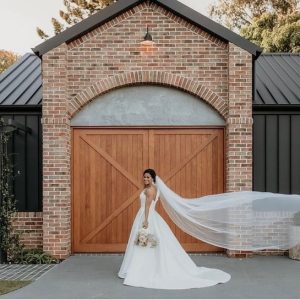A bride poses in front of a rustic brick building with large wooden doors