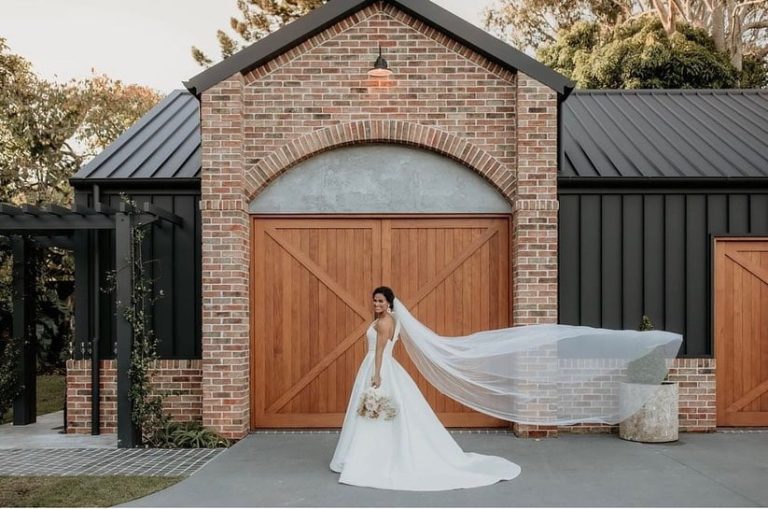 A bride poses in front of a rustic brick building with large wooden doors