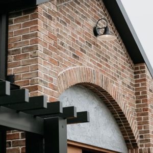 A black barn-style wall light is mounted on a brick wall above an arched entryway