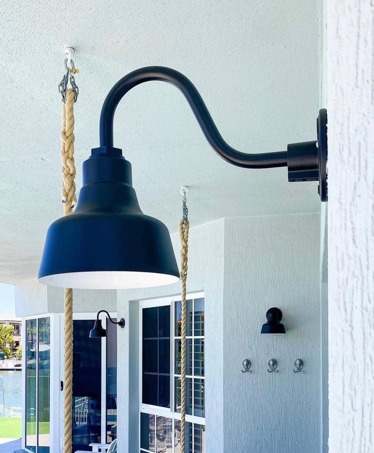 A large dark blue gooseneck barn light fixture hangs from a ceiling chain next to a large window