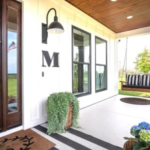 A modern farmhouse porch features a black gooseneck wall light illuminating the entrance