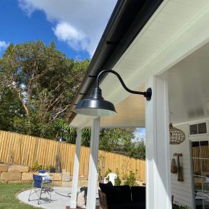 A black gooseneck barn light fixture is mounted under the eaves of a white outdoor patio