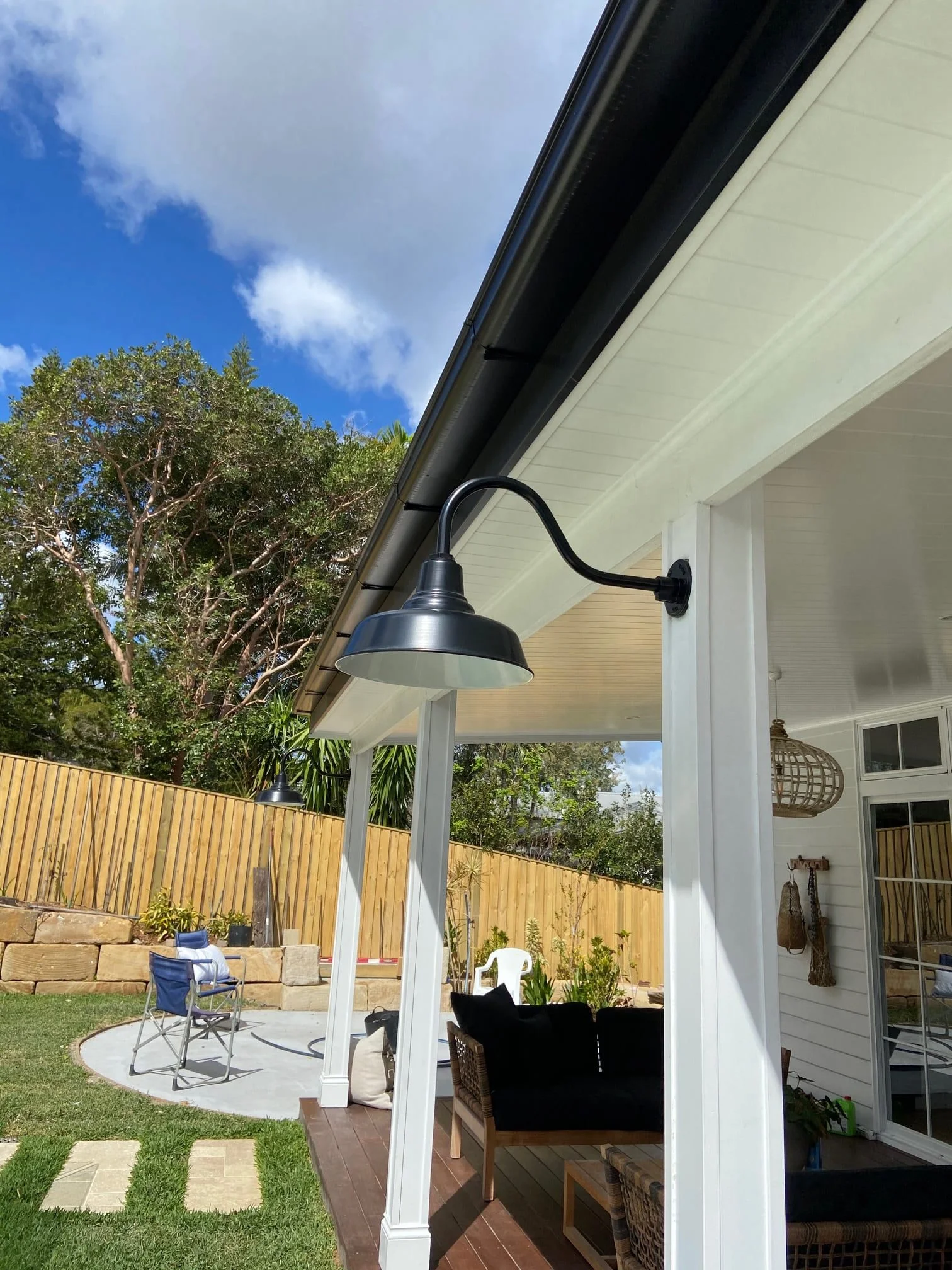 A black gooseneck barn light fixture is mounted under the eaves of a white outdoor patio