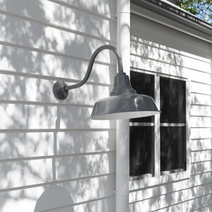 A grey gooseneck barn light is mounted on the white weatherboard exterior of a building