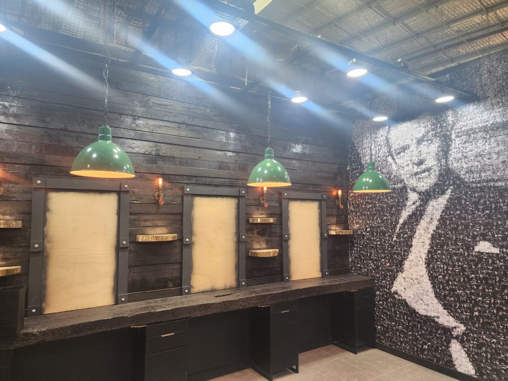 Three green pendant lights hang in front of a dark wood paneled wall with a large black and white portrait on the right