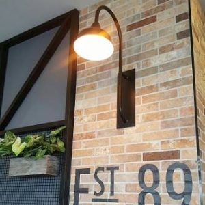 A black gooseneck wall light is mounted on a brick wall with 'EST 89' painted on it