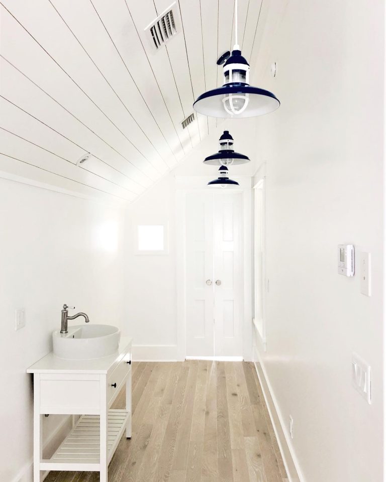 Three navy blue pendant lights hang in a bright, white hallway with a sink and vanity