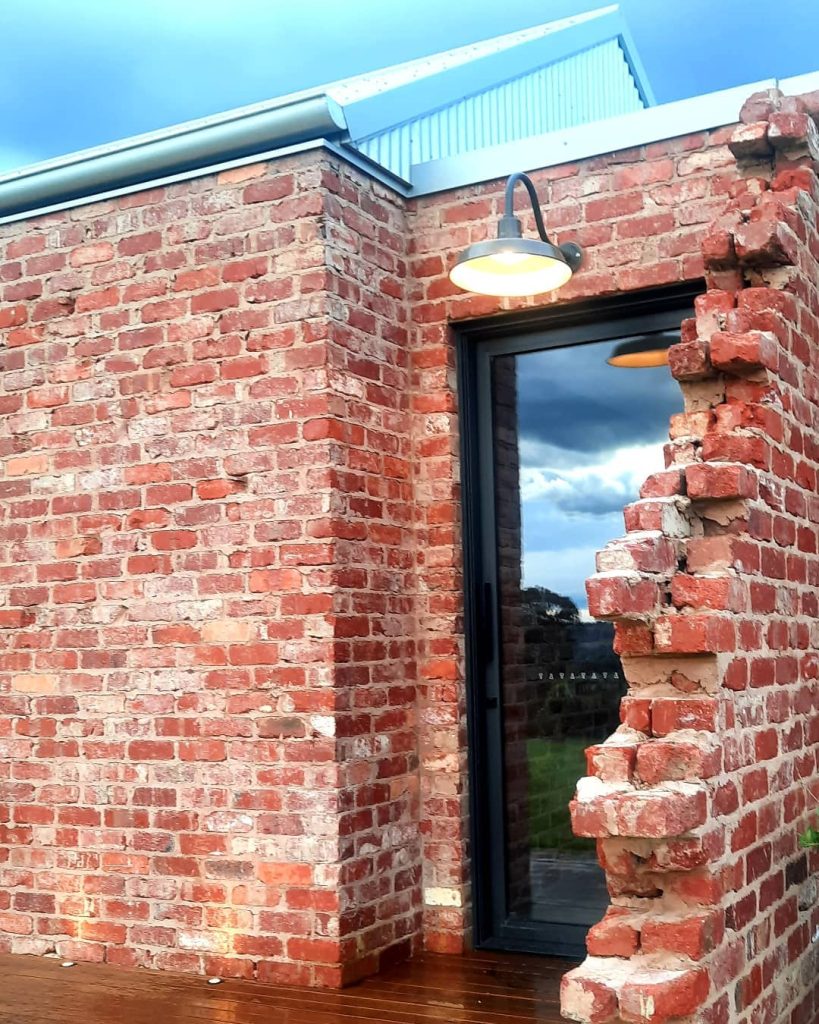 A gooseneck wall light illuminates the exterior of a rustic brick building