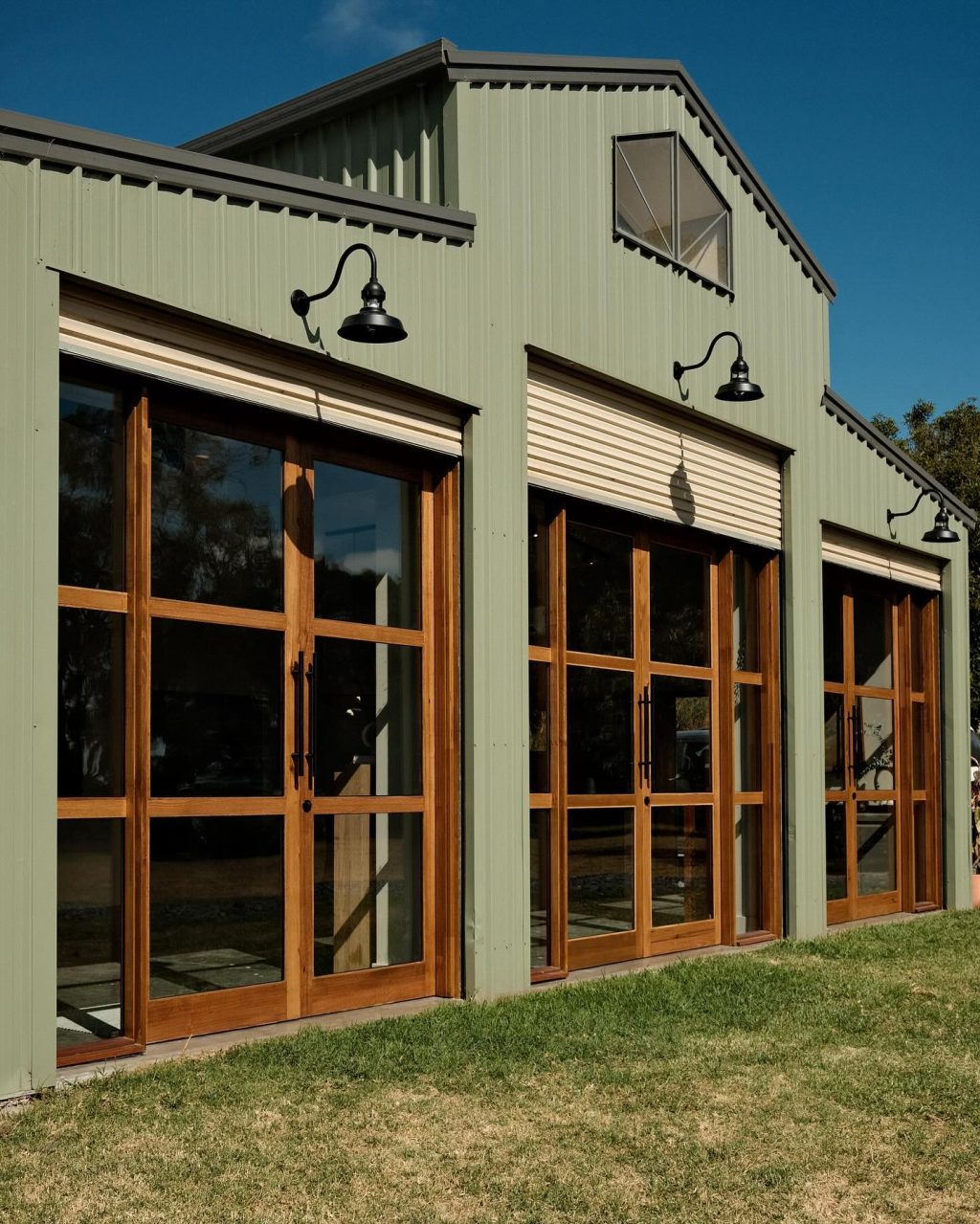 Three 30cm Sydney caged gooseneck barn lights in Black Ace on a sage green barn shed