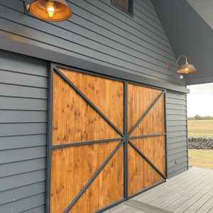 Two barn-style wall lights illuminate a modern home with dark grey siding and large wooden barn doors