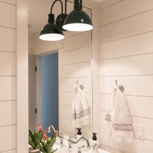 A dark green barn-style vanity light fixture illuminates a bathroom vanity with a marble countertop