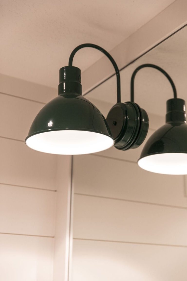 A dark green double wall light with gooseneck arms illuminates a shiplap wall