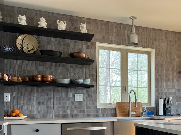 A modern kitchen features a grey tiled backsplash, open shelving with decorative items, and a pendant light fixture above a sink