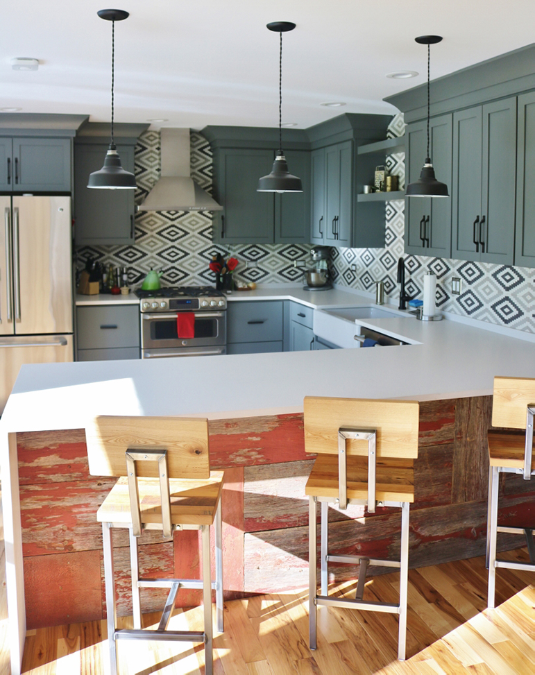 A modern kitchen features grey cabinetry, a geometric backsplash, and pendant lights above a breakfast bar