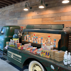 A vintage delivery truck is repurposed as a display for various products, illuminated by industrial-style wall lights