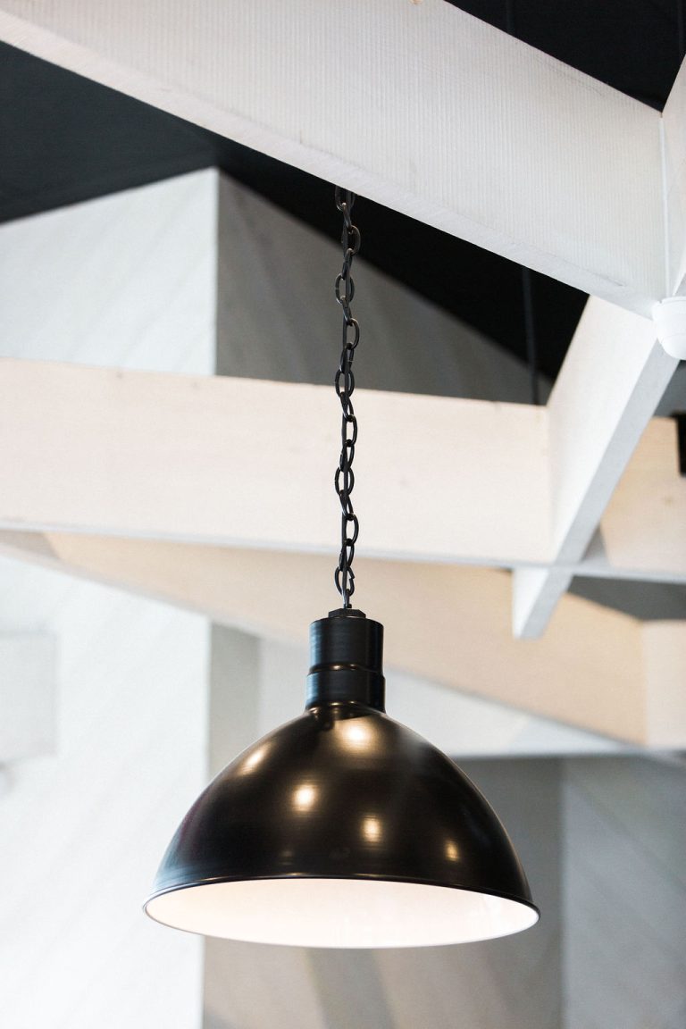 A black pendant light hangs from a chain against a backdrop of white beams