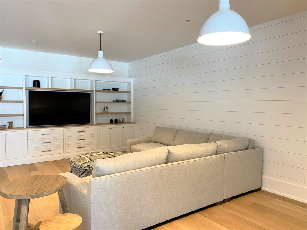 Two white pendant lights hang from the ceiling in a modern living room with a sectional sofa and built-in entertainment unit
