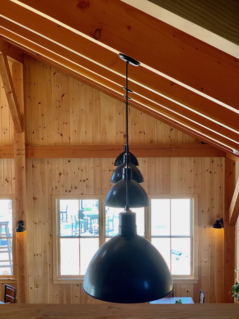 A large black pendant light hangs from a wooden ceiling in a room with wood-panelled walls and windows
