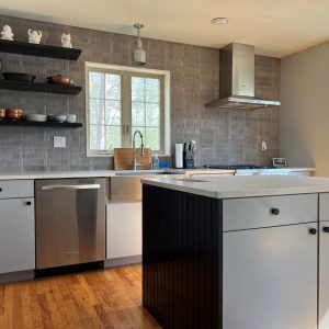 A modern kitchen features a grey tiled backsplash, stainless steel appliances, and a central island