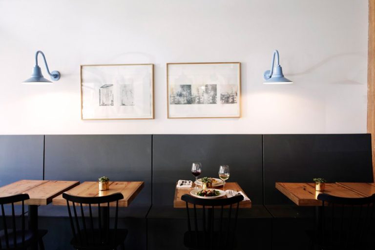 Two light blue gooseneck wall lights illuminate a dining area with wooden tables and dark seating
