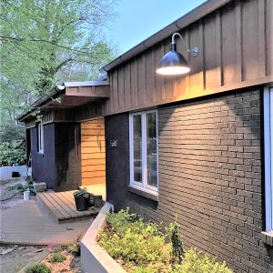 A dark gooseneck barn light illuminates the exterior of a modern home with brick and wood siding