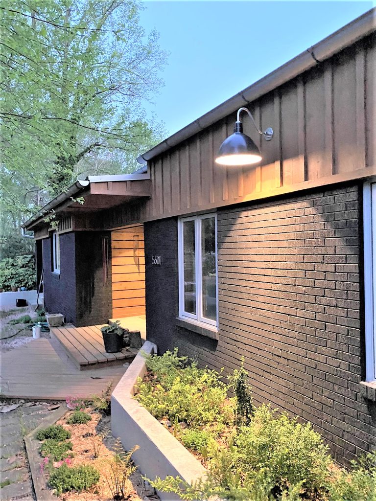 A dark gooseneck barn light illuminates the exterior of a modern home with brick and wood siding