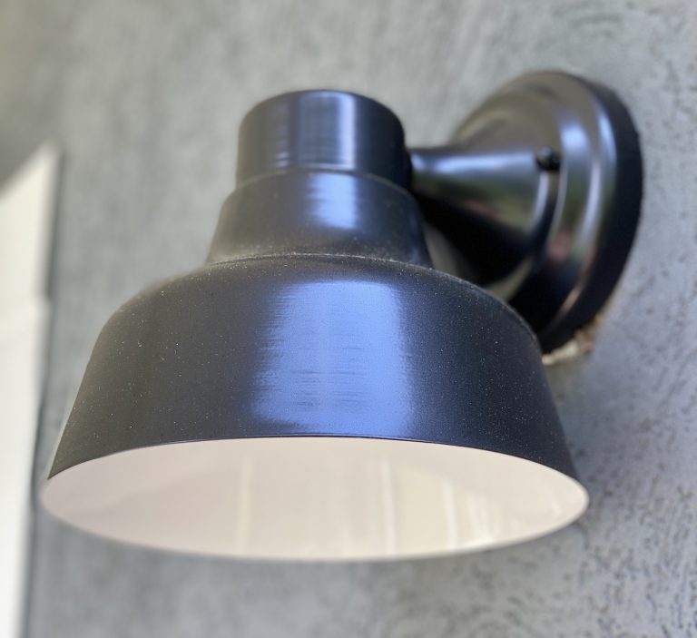 A black outdoor wall light with a white interior is mounted on a textured grey wall